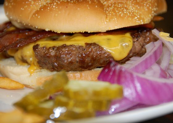 A cheeseburger with bacon, red onion and pickles on a sesame bun.