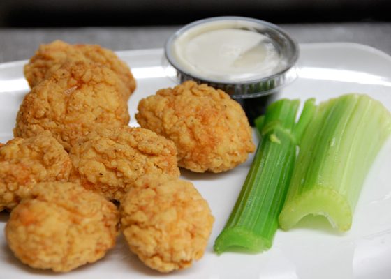 Breaded chicken nuggets on a plate with ranch dip and celery sticks.
