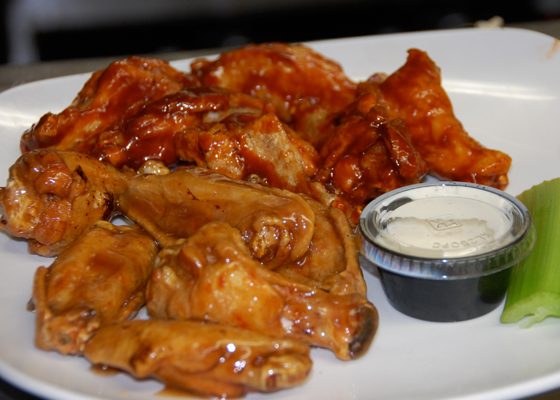 A plate of sauced wings with a cup of ranch and celery sticks.
