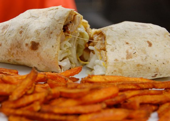 A wrap cut in half, served with sweet potato fries.